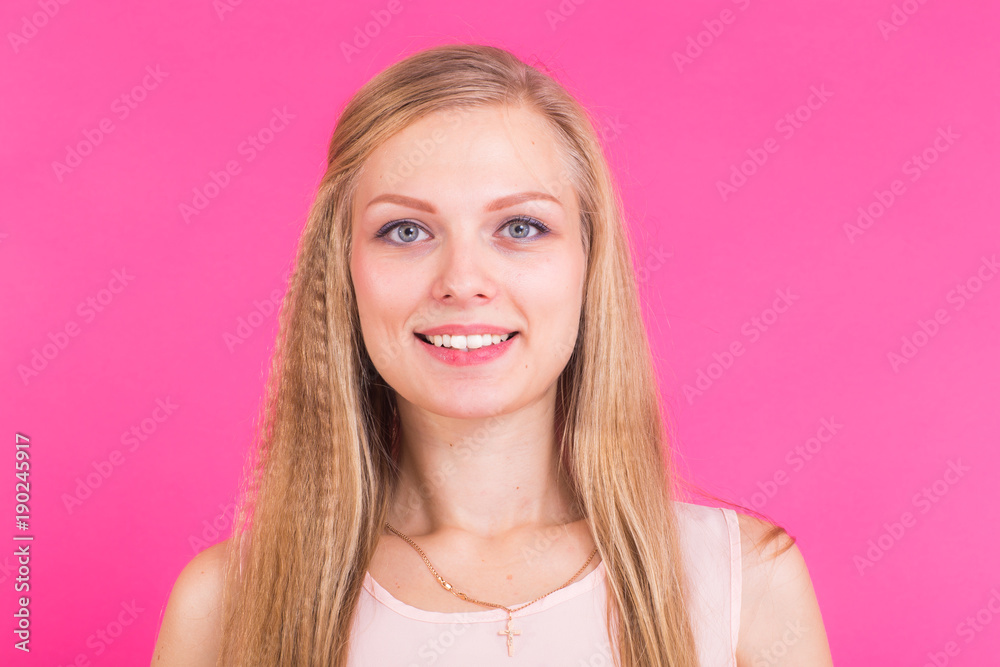Pretty young woman smiling against a pink background.