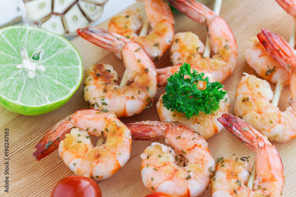 Skewers shrimp barbecue served on wood cutting board with lemon or lime in close up view. Delicious grilled prawn with spices for snacks in party. Homemade food concept of seafood menu. Skewers shrimp barbecue served on wood cutting board with lemon or lime in close up view. Delicious grilled prawn with spices for snacks in party. Homemade food concept of seafood menu.