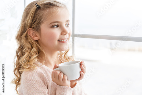 adorable little child drinking tea and looking through window