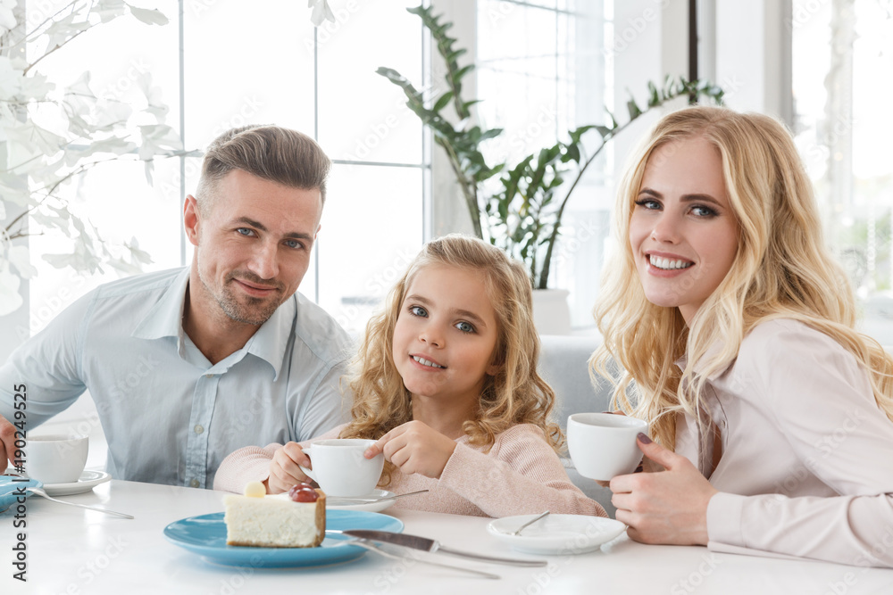 young family with coffee cups and cake spending time in cafe