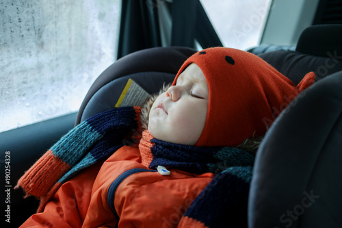 the boy is sleeping in the car seat in the winter