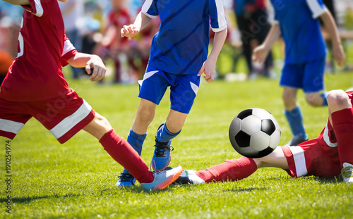 A group of young soccer players runnng the ball. Footballer dribbling drills and tackle attempt. Boys in red and blue jersey shirts playing football match