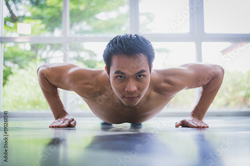 Asian muscular guy doing push-ups exercise on the floor