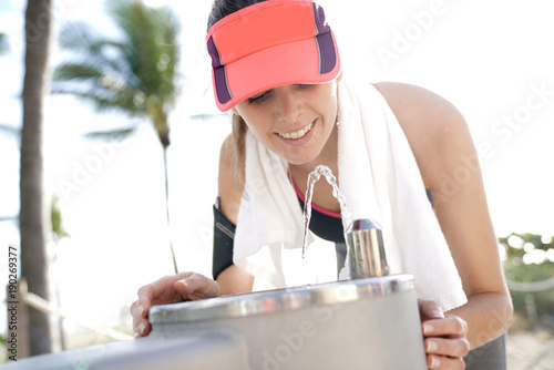 Obraz na plátně Fitness girl drinking from water fountain after exercising