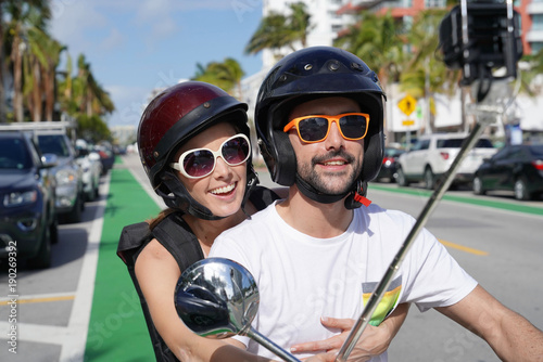 Couple riding scooter and filming themselves with small camera