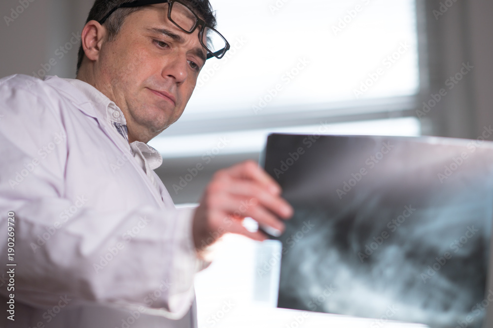 Doctor wearing a white lab coat examining X-ray images