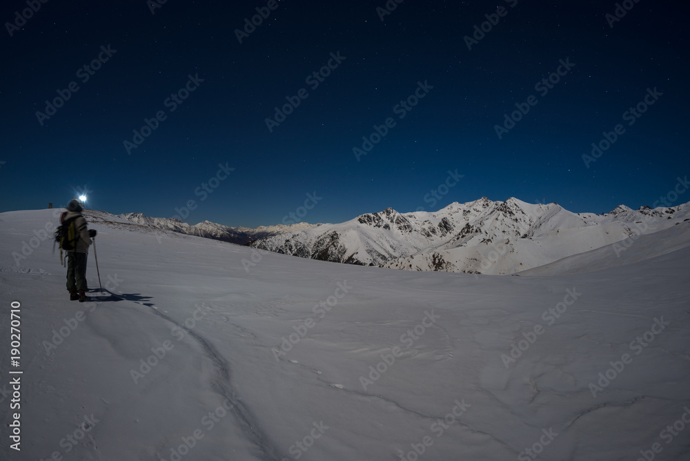 Snow on the Alps illuminated by moonlight, fisheye lens. Long exposure blurred two hikers looking at view, night outdoor activities. Snow on the Alps illuminated by moonlight, fisheye lens. Long exposure blurred two hikers looking at view, night outdoor activities.