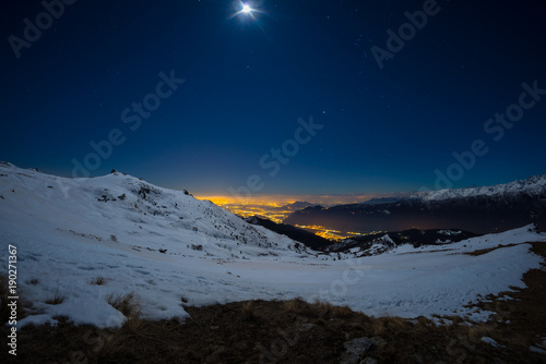 Turin city lights  night view from snow covered Alps by moonlight. Moon and Orion constellation  clear sky. Italy.