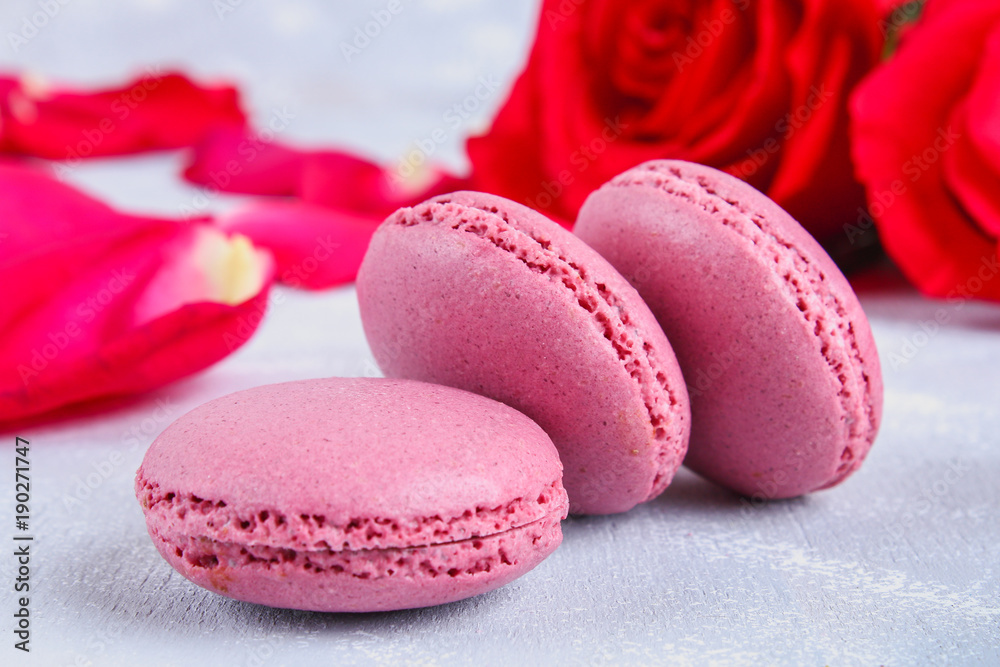 Pink and purple macaroons on a gray table surrounded by pink and white flowers. Pink and purple macaroons on a gray table surrounded by pink and white flowers.