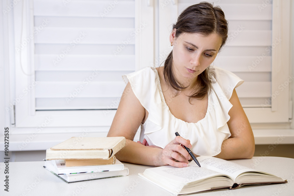 Young attractive female student with books is preparing for exams at university. Learn lessons. Education at home. Schoolgirl reading books at University of disciplines. Young attractive female student with books is preparing for exams at university. Learn lessons. Education at home. Schoolgirl reading books at University of disciplines.