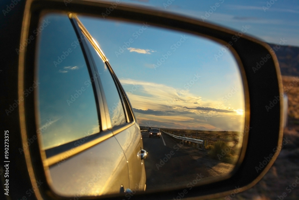 Reflection of colorful sunset. Side-view mirror during a journey. Driving at high speed on highway.