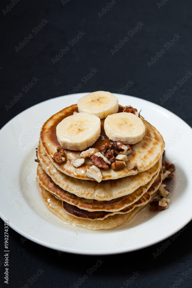 Pancakes with nuts, honey and banana in a plate on a dark background Menu , restaurant recipe concept. Served in Pancakes with nuts, honey and banana in a plate on a dark background Menu , restaurant recipe concept. Served in
