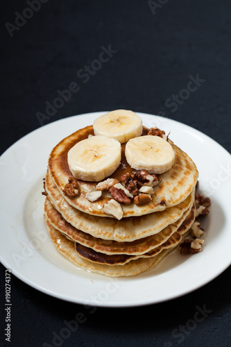 Pancakes with nuts, honey and banana in a plate on a dark background Menu , restaurant recipe concept. Served in