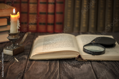 On the wooden background of the table there are stacks of colorful books near the old candlestick with burnt matches lying next to each other.