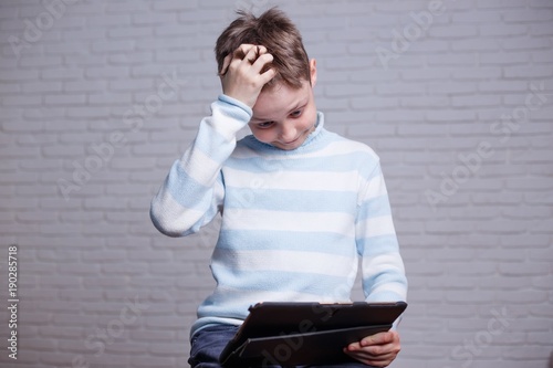 Pensive stressed bewildered boy with tablet. Gadget, internet addiction and technology concept photo