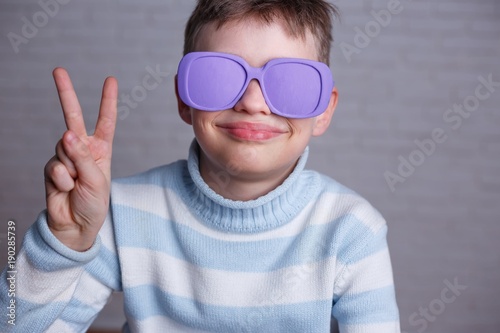 Cute smiling boy in violet sunglasses with opaque lenses showing victory gesture