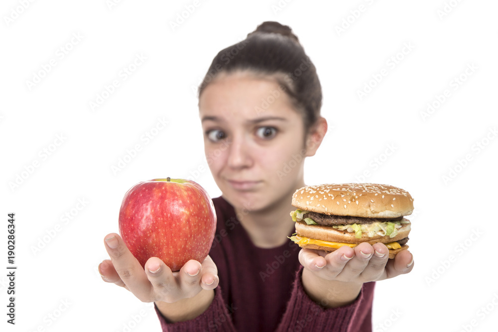 Adolescent girl choosing between fruit and a hamburger on a white background