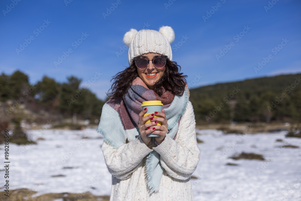 portrait of a young beautiful woman in the snow holding a cup of coffee or tea. Sunny weather. Wearing warm clothes. Lifestyle portrait of a young beautiful woman in the snow holding a cup of coffee or tea. Sunny weather. Wearing warm clothes. Lifestyle