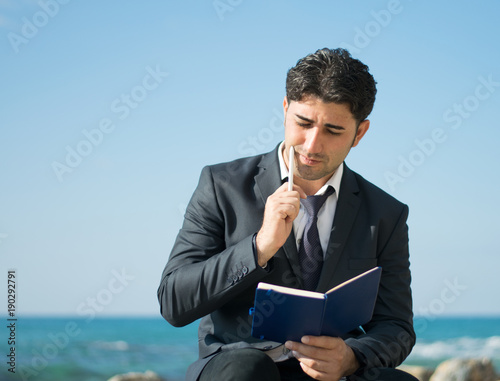 A freelance businessman is planning his work. A man on the sea writes in a notebook and thinks.