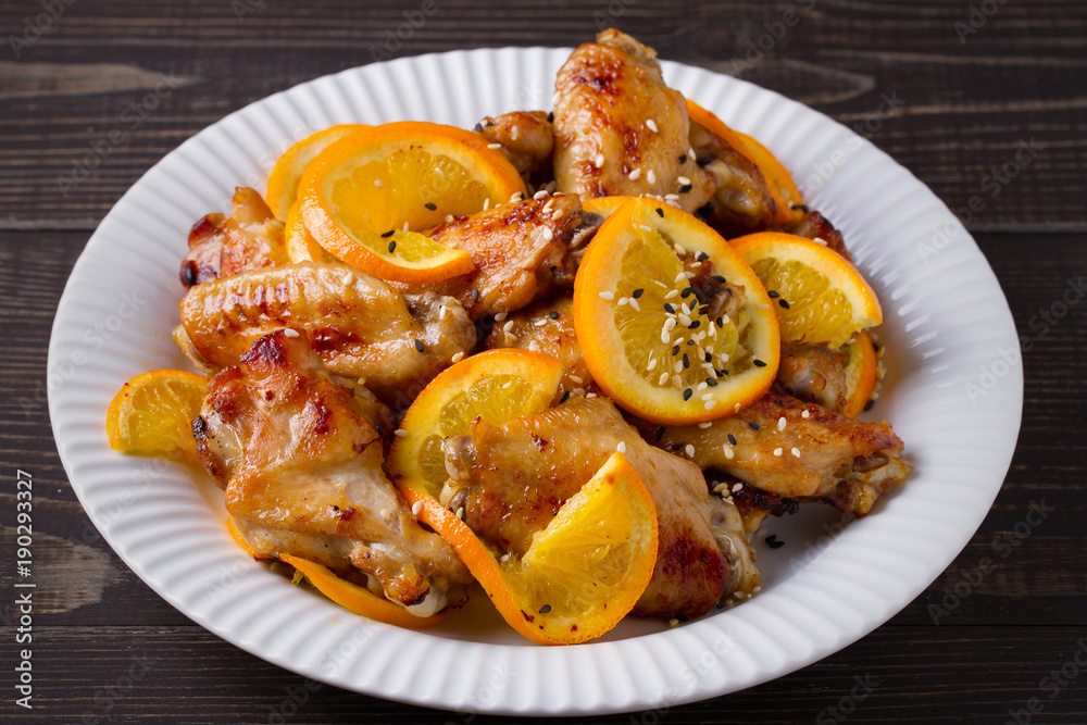 Sweet and sour chicken wings with oranges, served with sesame on white plate Sweet and sour chicken wings with oranges, served with sesame on white plate