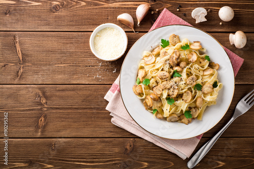 Tagliatelle pasta with mushrooms, parsley and Parmesan cheese on wooden table.