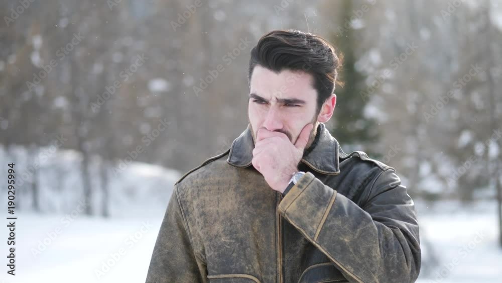 Handsome tired young man posing among snowy woods in the mountain yawning, wearing leather winter jacket Handsome tired young man posing among snowy woods in the mountain yawning, wearing leather winter jacket