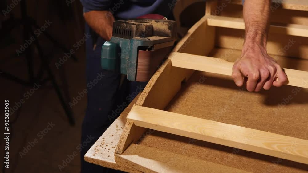 close up shot of the men's hands, who uses a tool to smooth out the wooden surface of furniture that he creates in his workshop for working with sawn timber close up shot of the men's hands, who uses a tool to smooth out the wooden surface of furniture that he creates in his workshop for working with sawn timber