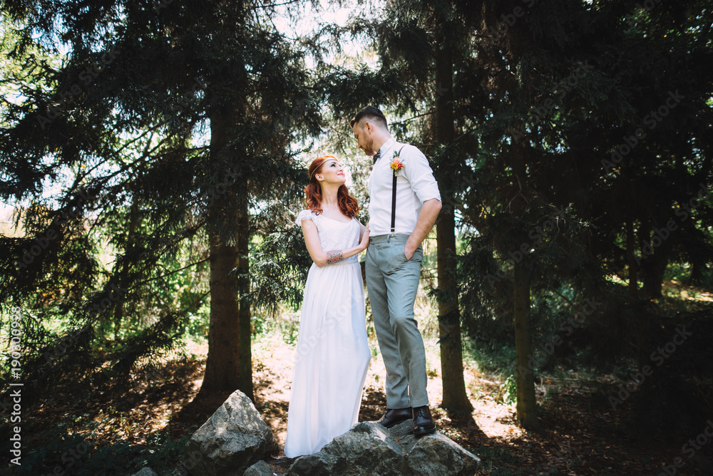 Beautiful young couple in a forest. They stand on a large stone and look at each other