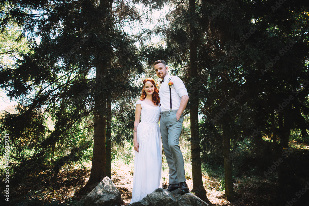 The newlyweds stand on a large stone in the forest. They are in wedding dresses The newlyweds stand on a large stone in the forest. They are in wedding dresses