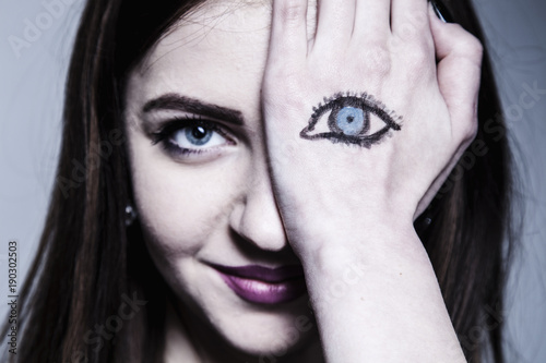 Staring brunette woman with painted eyes on her hand as a symbol of not fair play and double standards (gestures, body language, psychology concept)