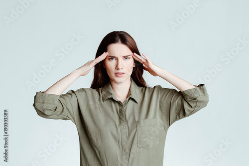 Young beautiful woman brunette holding fingers on temples frowning from pain over white background. Headache.