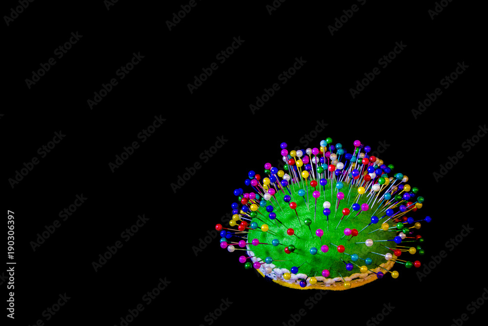 Pincushion with colorful pins on a black background.