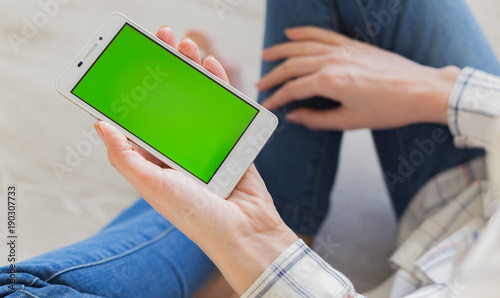 Woman at home relaxing reading on the smartphone with pre-keyed green screen 