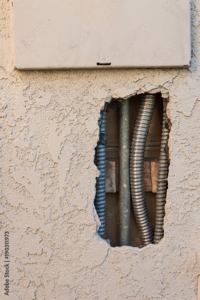 View of electrical conduit seen through a hole in the exterior stucco