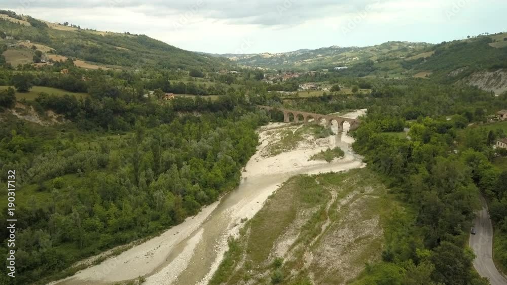 The white limestone area in the mountain area in Italy with the long bridge in the middle and the tall trees on the side The white limestone area in the mountain area in Italy with the long bridge in the middle and the tall trees on the side