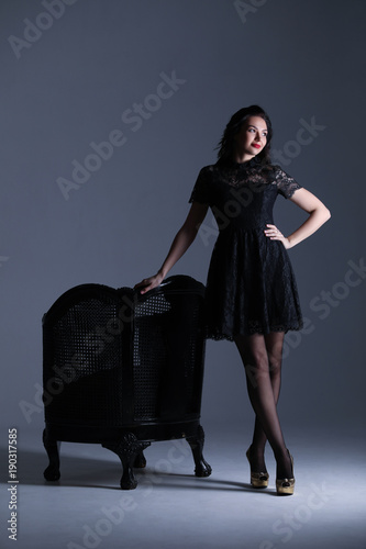 Model with long legs posing near the antique chair. Gray background. Photographie retouchee