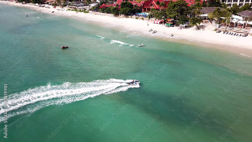 Aerial view of white sand beach and jet ski on the blue lagoon aqua sea. Aerial bird's eye view of jet ski cruising in high speed in turquoise clear water sea