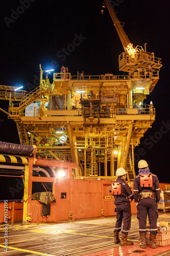 Two worker in offshore oil and gas operation discussion about platform before transfer to working on platform in night ship during stand in supply boat