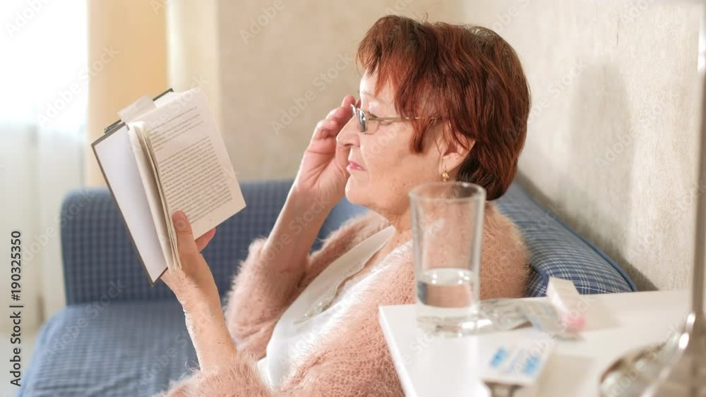 Old woman reading a book on the couch at home