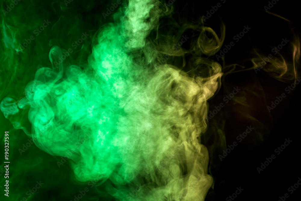 Thick colorful smoke of   green and yellow on a black isolated background. Background from the smoke of vape
