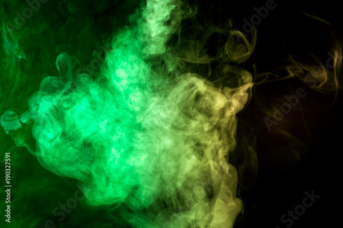 Thick colorful smoke of green and yellow on a black isolated background. Background from the smoke of vape