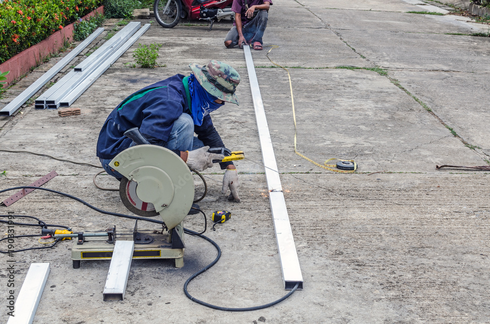 Asian worker with machine cutting metal and welded steel to create a roof, local labor construction concept