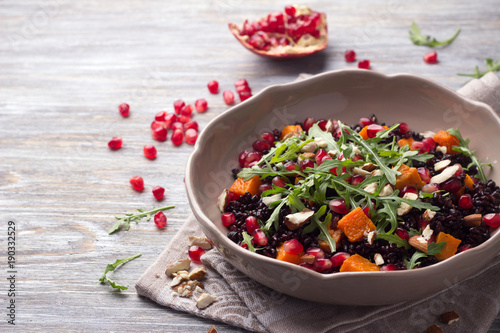Salad with black rice, baked pumpkin, pomegranate seeds, arugula and nuts on a gray background. Delicious vegan food