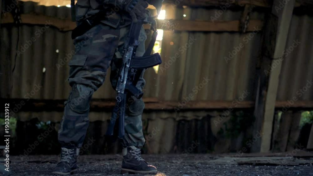 A combatant in army fatigues takes a rifle from the shoulder. A combatant in army fatigues takes a rifle from the shoulder.