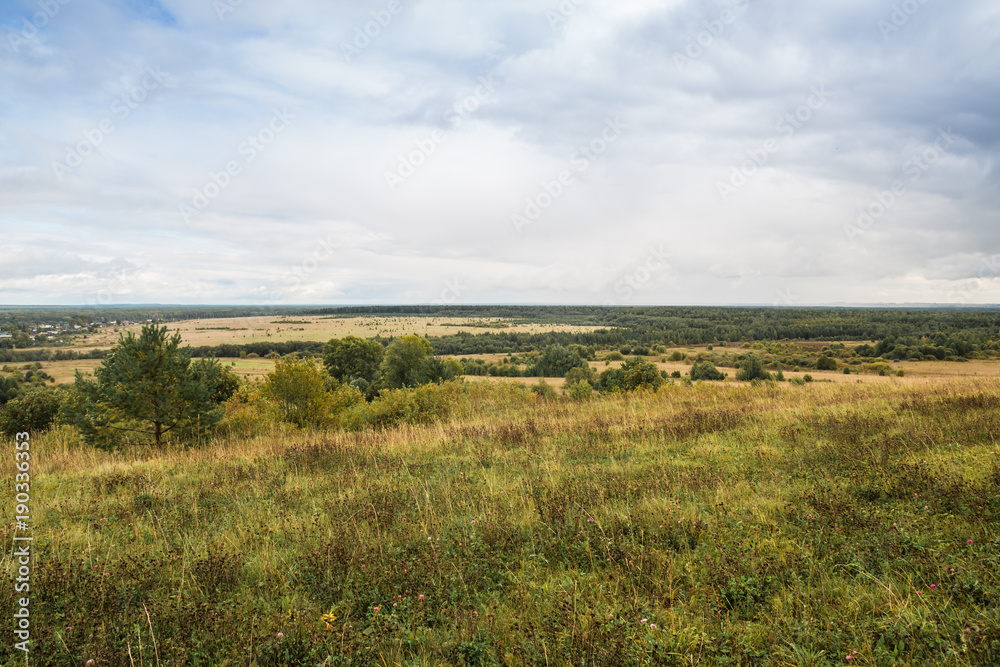 View from the height on the field, trees and river in the distance in autumn day