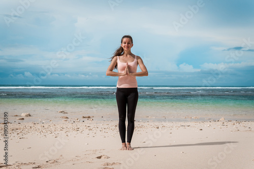 Fitness woman in sports clothing practicing yoga with namaste, ocean background