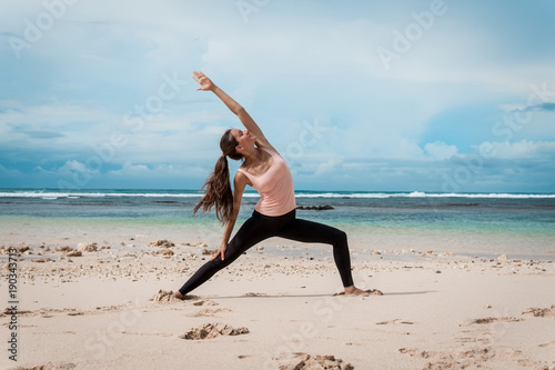 Woman doing yoga on coast of ocean on beach