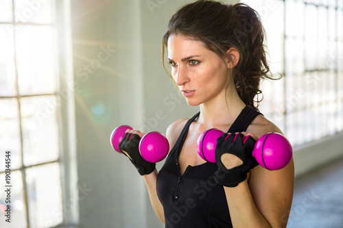 Confident serious focused and confident female working out with weights at bright gym