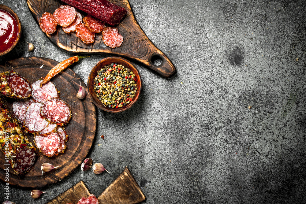 Different kinds of salami with spices and herbs on old boards. Different kinds of salami with spices and herbs on old boards.