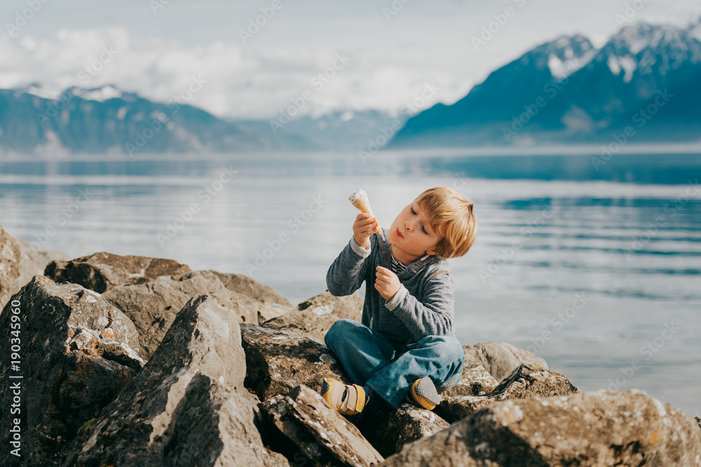 Cute little blond boy eating ice cream, resting by lake Geneva, Lausanne, Switzerland